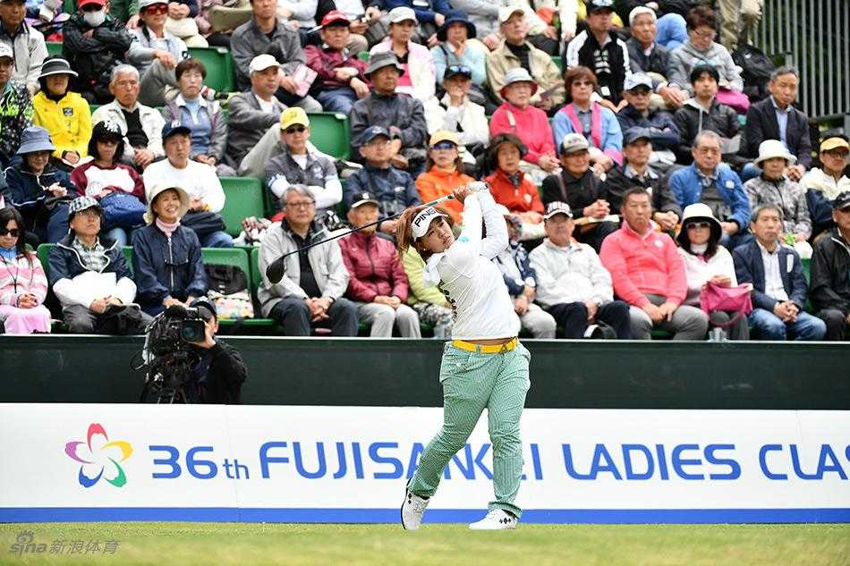 藤本麻子优雅走上果岭，阳光洒在她身上，与剪影般的观众共同构成一幅宁静而充满张力的画面。