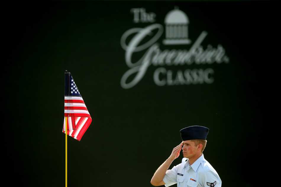从稍远视角观看整个致敬场景，国旗、卫兵、果岭与球场建筑构成和谐画面，展现出仪式整体的宏大与肃穆。