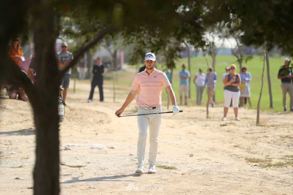 一位球员在强风中完成沙坑救球，沙粒被击打得飞扬起来。