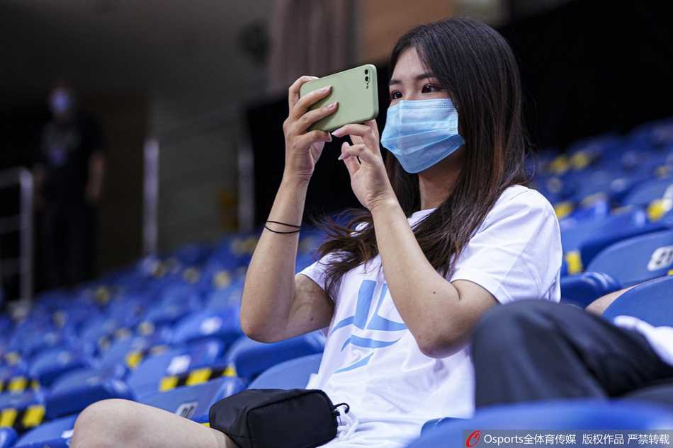 身穿黄色马甲的场馆工作人员正在引导一位女士进行入场前的身份核验，桌上摆放着消毒液和登记表，一丝不苟。