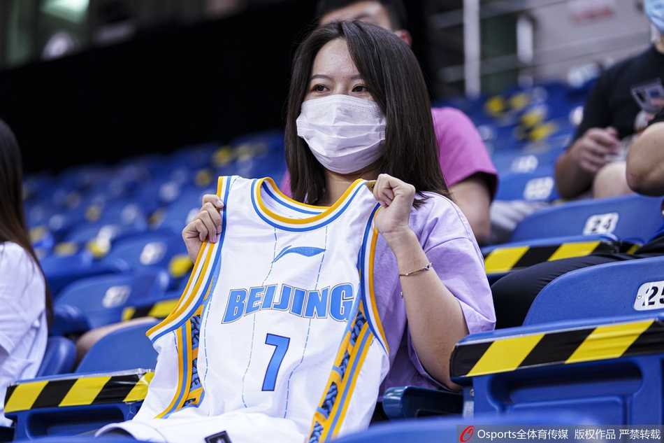 比赛间隙，镜头捕捉到一位年轻的女球迷，她戴着口罩，双手扶着栏杆，全神贯注地注视着场内激烈的拼抢。