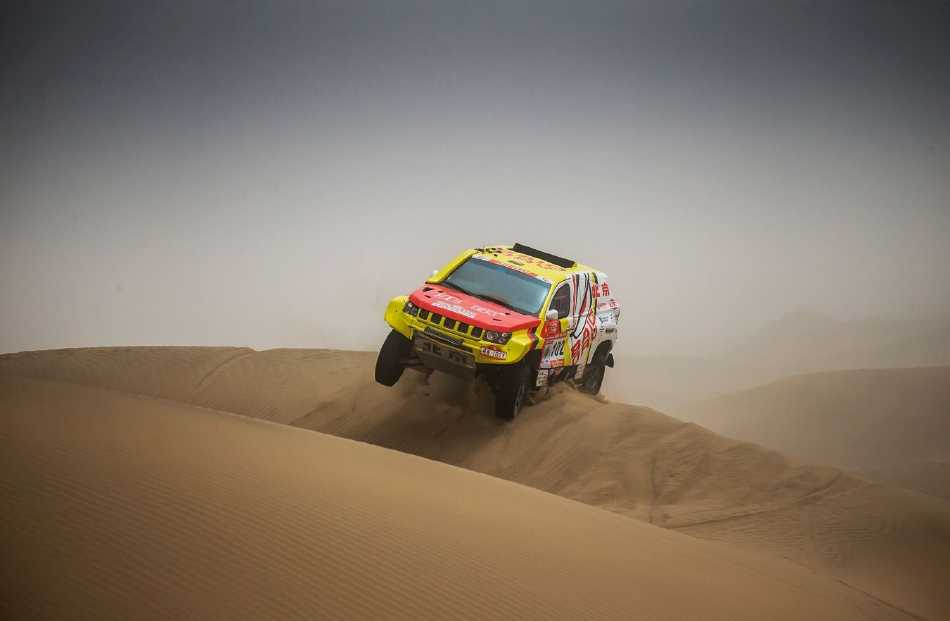 夕阳为无垠沙丘镀上温暖金边，一辆赛车剪影驶向远方，在苍茫天地间映照出人类探索未知的执着与浪漫。