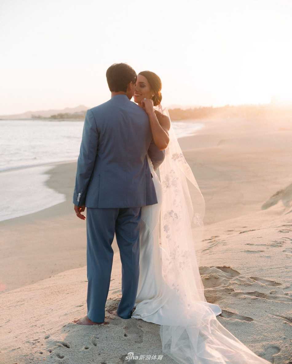 福勒与新娘斯托克在碧海蓝天下深情对视，新郎身着淡蓝色休闲西装，新娘一袭简约优雅的白色婚纱，宛如海风中的一对璧人