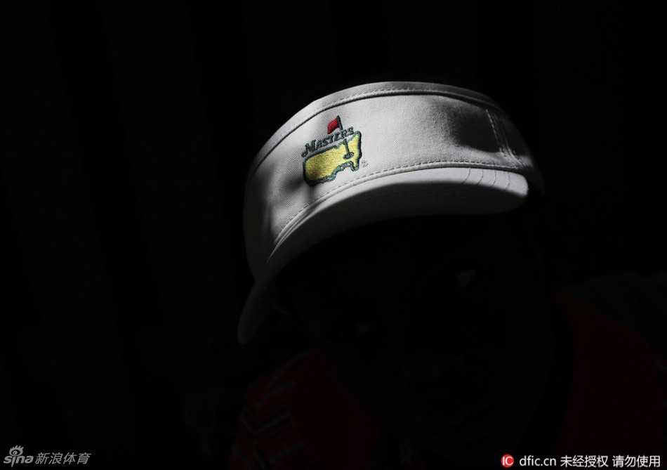 一位头戴经典绿色大师赛纪念帽、身着时尚条纹衫的女性球迷，正专注地望向远方，帽檐下是优雅而期待的侧影。