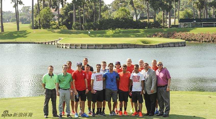 一位美国国足球员正在17号洞发球台全神贯注地准备挥杆，他的目光紧盯着远方水中央的果岭，姿态专注而有力。