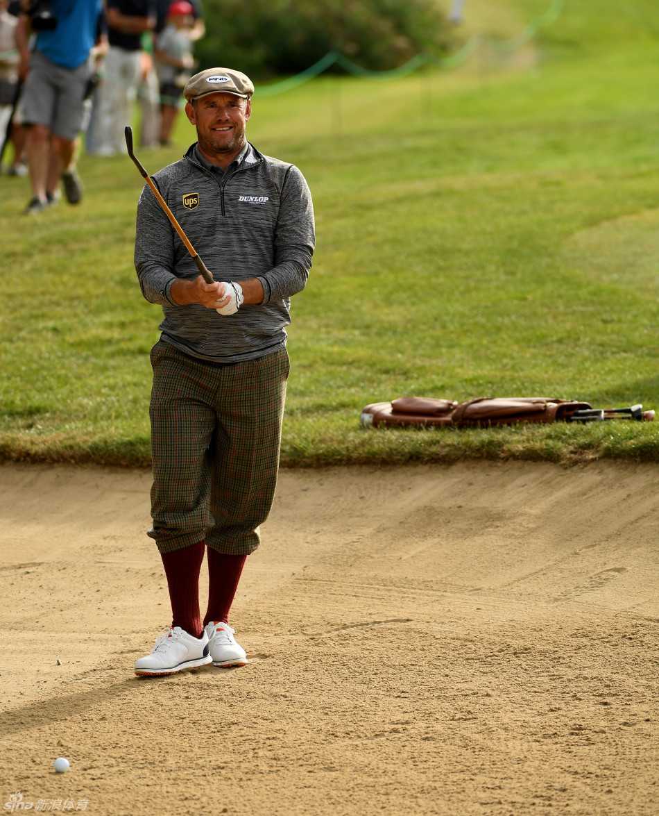 李·维斯特伍德手握经典木质杆头的复古球杆，在沙坑边全神贯注地审视球位，仿佛一位在研究战略的将领。