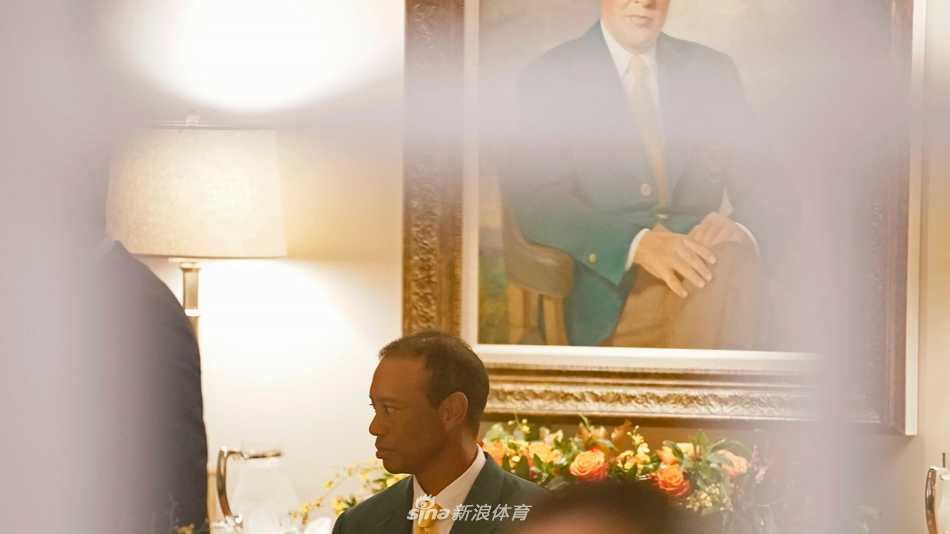 泰格·伍兹身着标志性红色 Polo 衫，手持葡萄酒杯，在冠军晚宴现场与往届冠军们亲切交谈，脸上洋溢着主人的从容微笑。