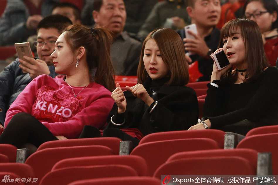 两位姑娘专注地盯着赛场方向，手中拿着助威棒，在喧闹的场馆中神情专注，眼中满是对赛场上那个身影的期盼与支持。