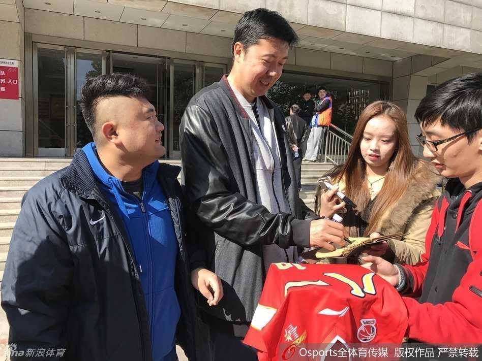 王治郅在训练馆中被热情的女球迷团团围住，他俯身倾听粉丝的话语，现场气氛热烈而融洽，展现了他超高的人气。
