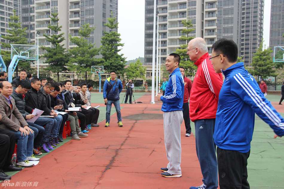 前男篮国手李群站在孩子们中间，正在耐心讲话布置训练任务，孩子们仰着头认真聆听