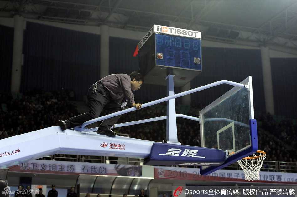 在漆黑的计时器下方，一名身穿工作服的技术人员站在梯子上，正仰头仔细检查着故障部件，而周围的灯光映照出他忙碌而无奈的身影。