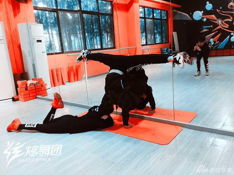 一名舞者正在进行基本功训练，她以墙为辅助，努力拉伸韧带，身体线条展现出柔韧与力量交织的独特美感。