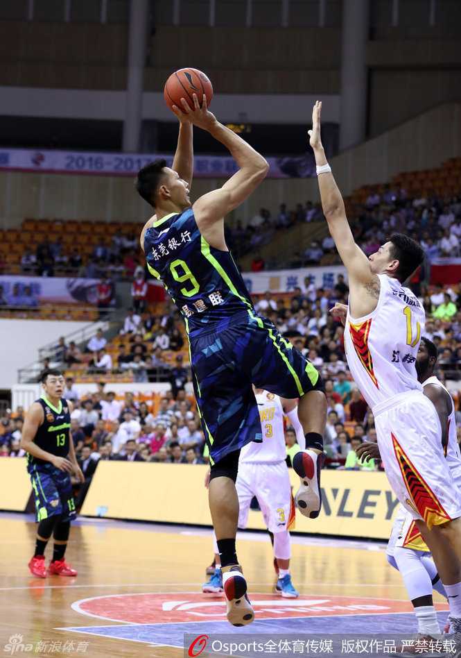 易建联在防守球员头顶高高跃起，使出了标志性的后仰跳投，身体在空中形成一道完美的弧线，眼神专注地盯着篮筐。