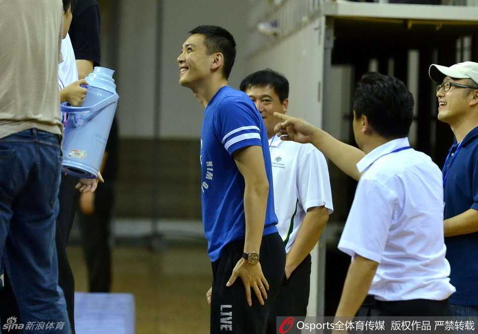 杨鸣手持水瓶，侧身与身旁的教练组成员认真交流，手指球场方向，似乎在探讨战术细节。