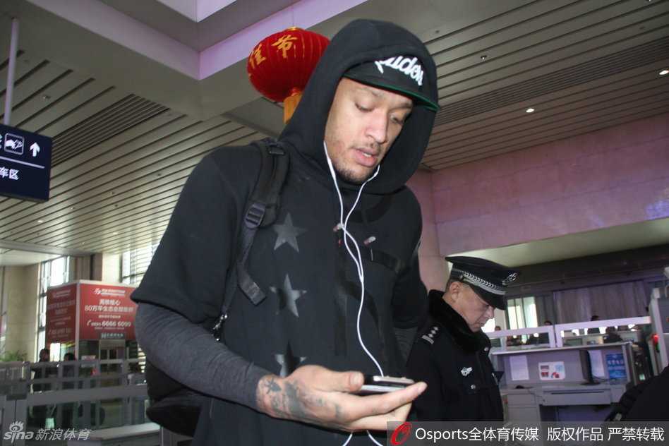 身穿红色外套的比斯利在高铁站入口处被热情球迷团团围住，他面带微笑耐心地俯身为身前的小球迷在篮球上签名，场面温馨动人。