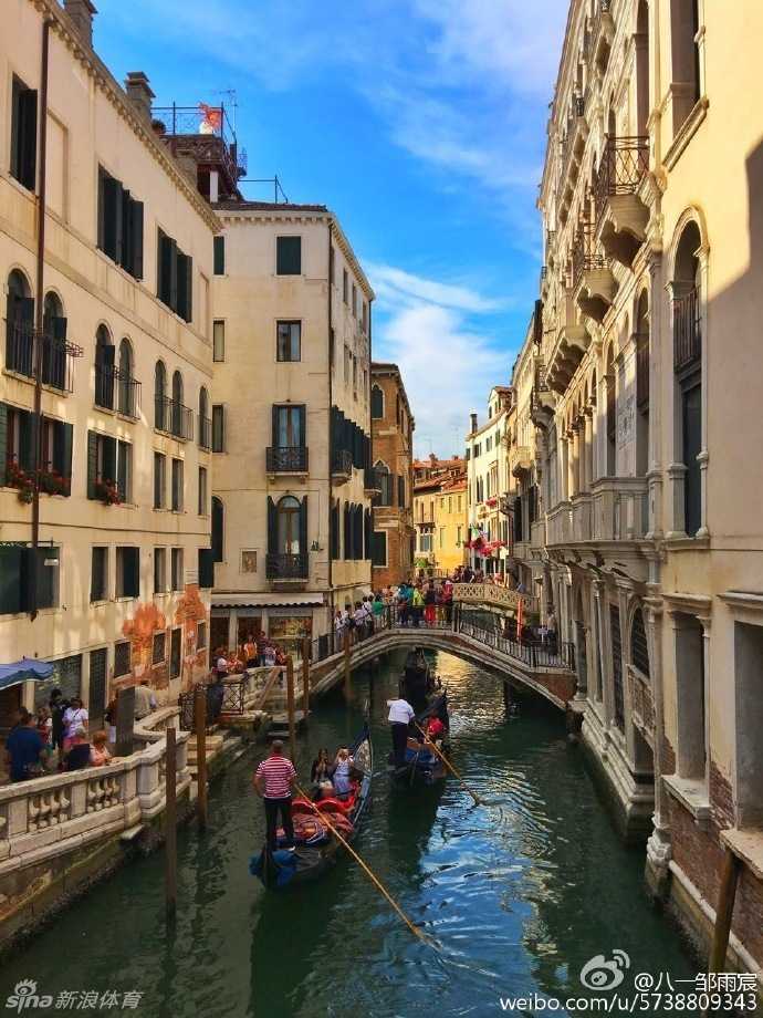 贡多拉游船静静停泊在运河岸边，远处的安康圣母教堂穹顶在夕阳下泛着金光，邹雨宸用手机记录下这一刻的水城风情。