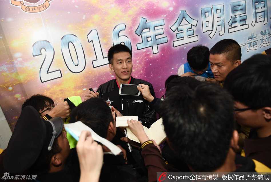 辽宁球星郭艾伦身穿北区蓝色球衣，被一群热情的球迷团团围住，他脸上笑开了花，眼睛眯成一条缝，正低头为一位球迷手中的纪念品签名。