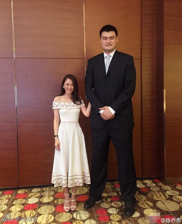 成龙大哥身穿白色唐装，抱拳微笑，气宇轩昂，背景粉丝高举灯牌，欢呼声此起彼伏。