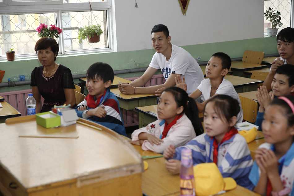 翟晓川俯身将崭新的书包递到小同学手中，孩子脸上绽放出腼腆而灿烂的笑容，仿佛接过了一份沉甸甸的未来