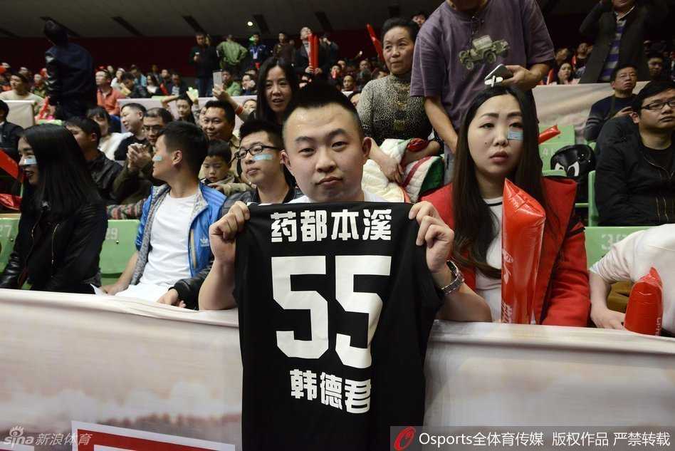 一位面容轮廓与辽宁队中锋韩德君惊人相似的辽宁男球迷，身着白色助威T恤，在四川球迷的包围圈中神情坚毅，仿佛就是大韩本人在场边坐镇，为球队注入无形力量。
