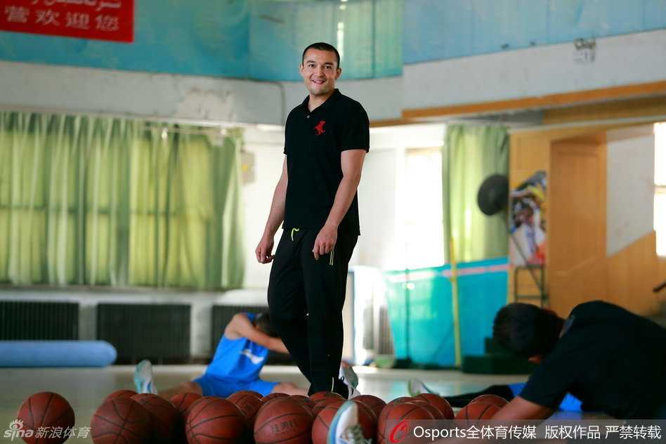 外籍教练在一旁辅助教学，西热力江双手抱胸，神情专注而严肃，仔细观察着场上的训练环节