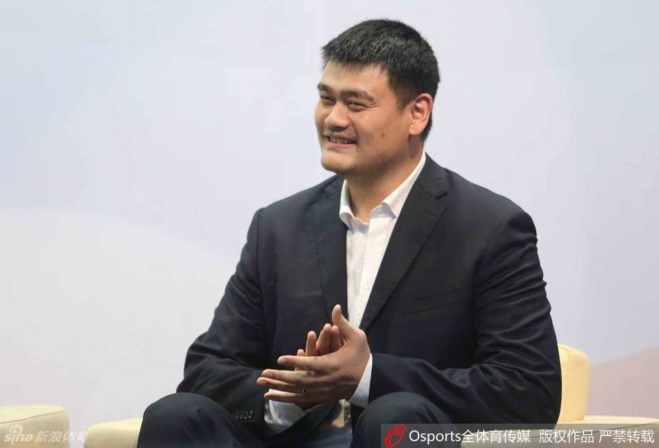 姚明身着深色西装，认真倾听台上发言，嘴角微微上扬，眼神中透露出对论坛观点的思索与兴趣。