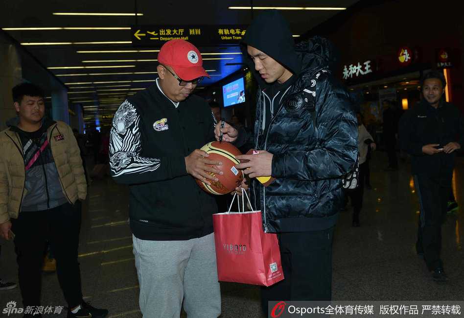 郭艾伦面带亲和微笑，俯身为小球迷在辽宁队球衣上签名，周围满是羡慕与喜悦的目光