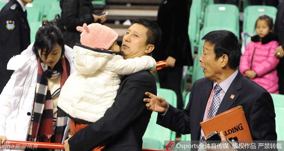 一家三口背影，郭士强一手抱娃一手牵着妻子，三人背影在空旷球馆灯光的拉长下显得格外温馨坚定