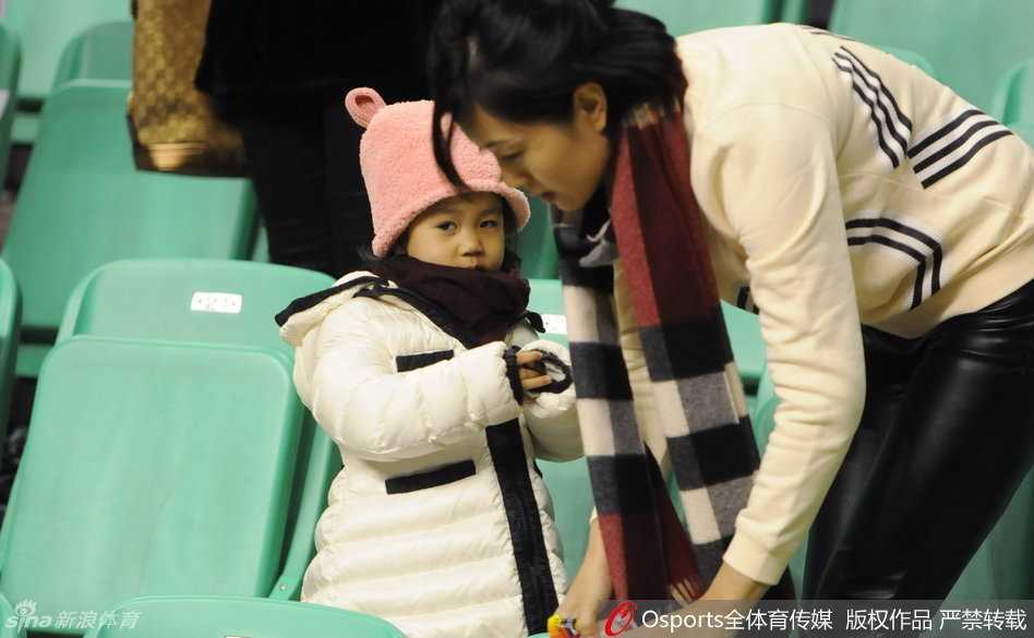 郭士强紧紧怀抱着年幼的女儿，眼神坚定地望向远方，妻子紧跟在身旁，三人在空旷的球场通道中缓步前行
