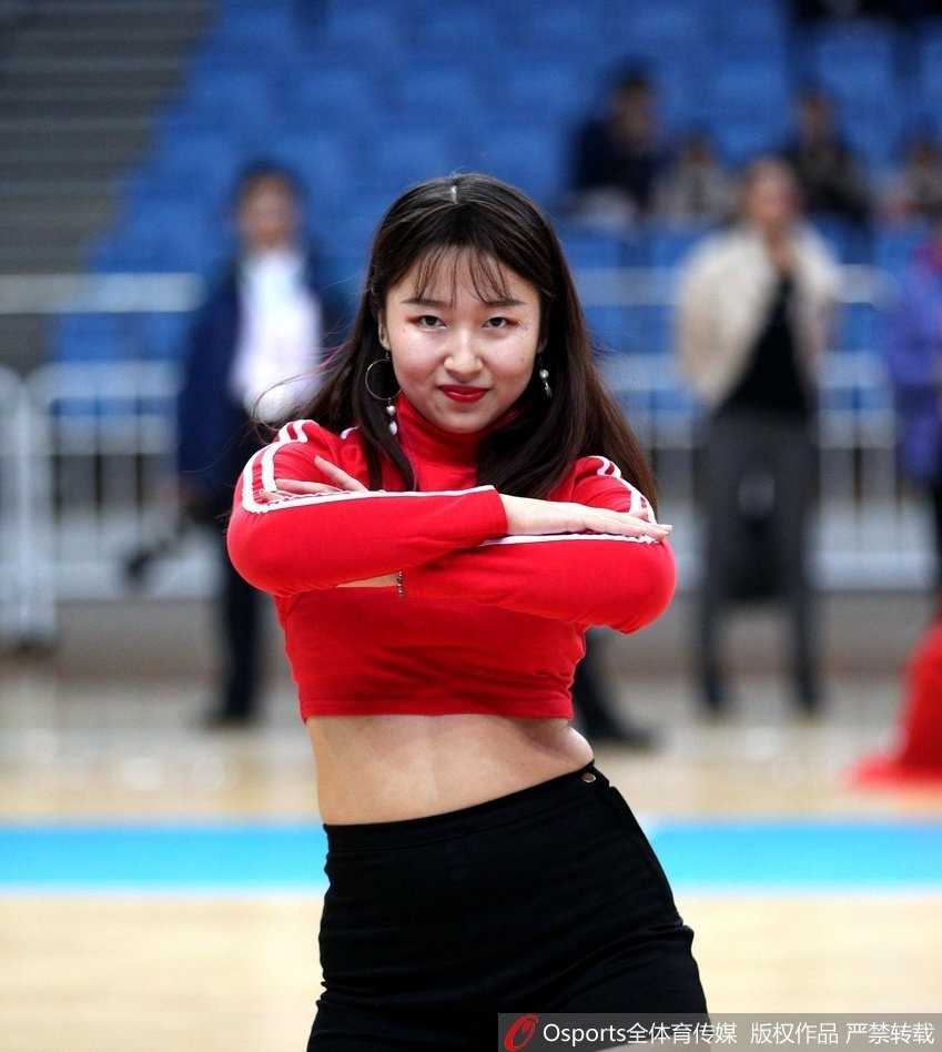 在灯光聚焦的球场中央，一名篮球宝贝高高跃起，飞舞的发丝和动感的舞姿定格在这一瞬间，展现出女性特有的力量与柔美之美。