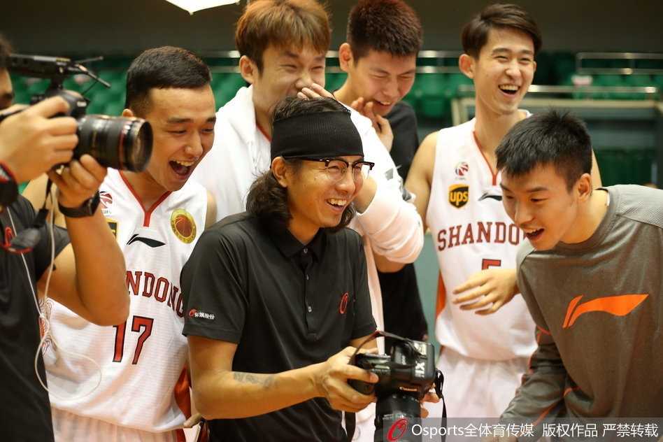 丁彦雨航被队友从身后紧紧锁喉，他的脸上露出既无奈又享受的笑容，而身后的队友则憋着坏笑，仿佛在密谋什么整蛊计划。