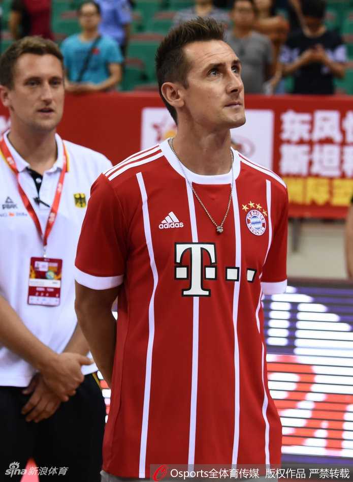 克洛泽在看台上专注地观看篮球比赛，他双手轻握置于膝上，侧脸的线条依然刚毅，眼神随着球场的攻防转换而移动，完全沉浸在比赛的紧张氛围中。