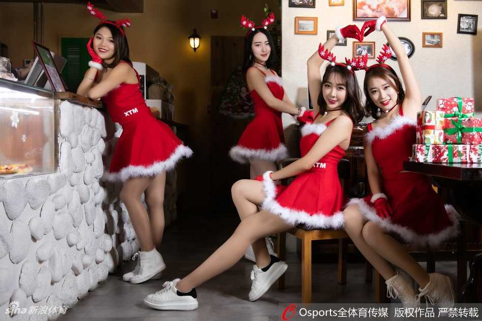 在明亮的体育馆通道内，一名啦啦队员双手抱满了装满礼物的红色袋子，对着镜头露出俏皮而神秘的表情，仿佛在告诉球迷们：“猜猜里面有什么惊喜？”红色的裙摆与节日的氛围相得益彰。