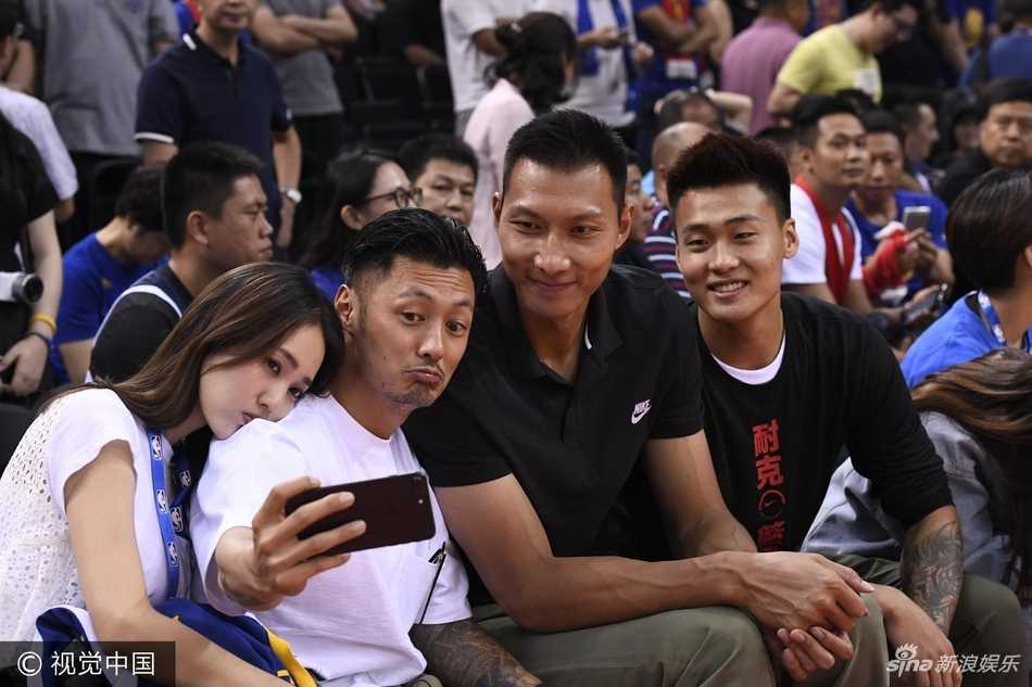 易建联身穿中国男篮球衣侧身看向前排，用手轻掩嘴角笑得腼腆，一旁的陈建州露出惊讶又玩味的表情