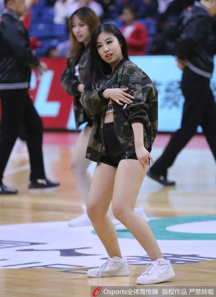 一位青岛啦啦队员在表演间隙独自站在场边，她扎着高马尾，若有所思地看向远方，身后的看台上坐满了热情的观众。这张照片展现了篮球宝贝在喧闹赛场中难得一见的安静与柔美。