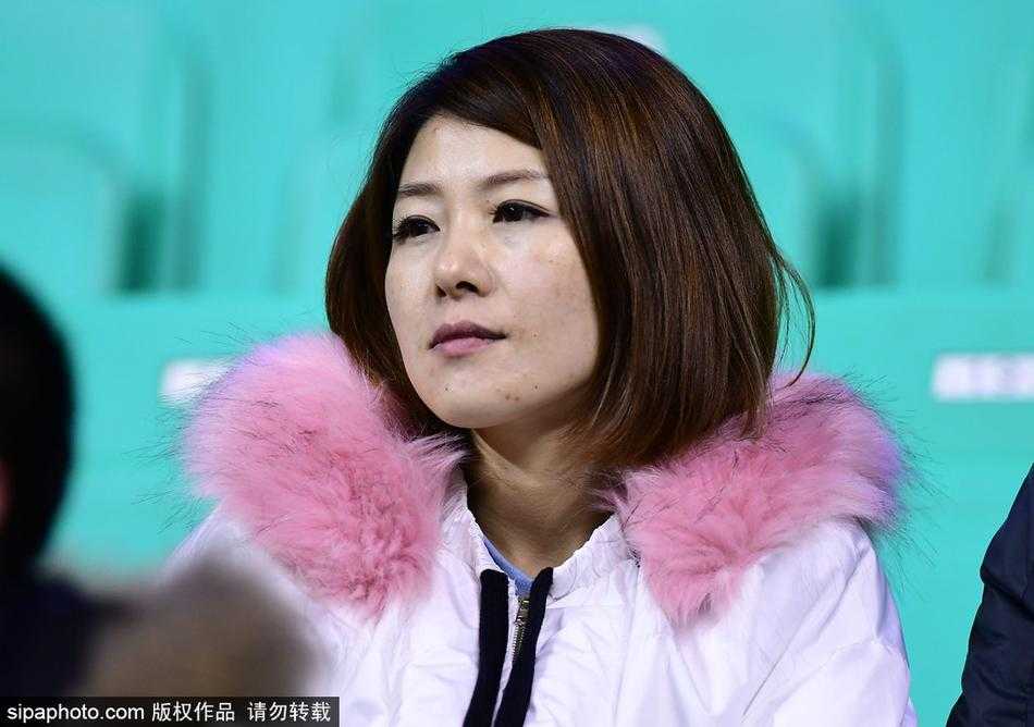 一位五官精致、眼神清澈的长发美女球迷，身着简约的白色休闲装，坐在人声鼎沸的辽宁本溪体育馆看台上，她的目光穿越喧嚣，温柔地聚焦在赛场中央，仿佛是喧嚣世界里的一股清流。