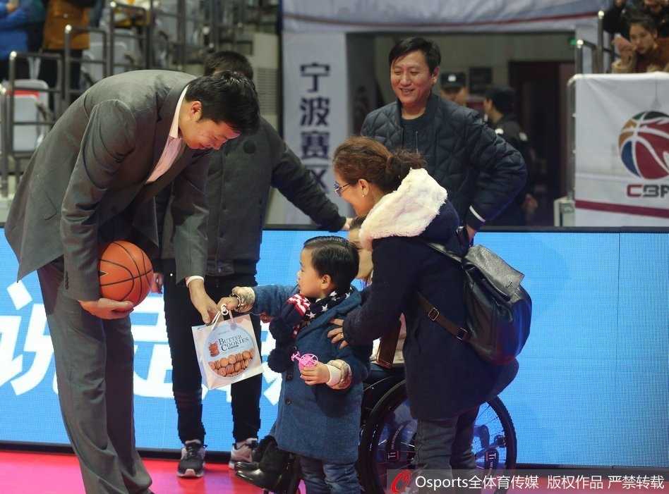 桑兰的儿子身穿可爱的羽绒服，坐在妈妈身边，他回头看向镜头，表情纯真。桑兰的手搭在儿子身上，母子二人与身后巨大的篮球海报相映成趣。