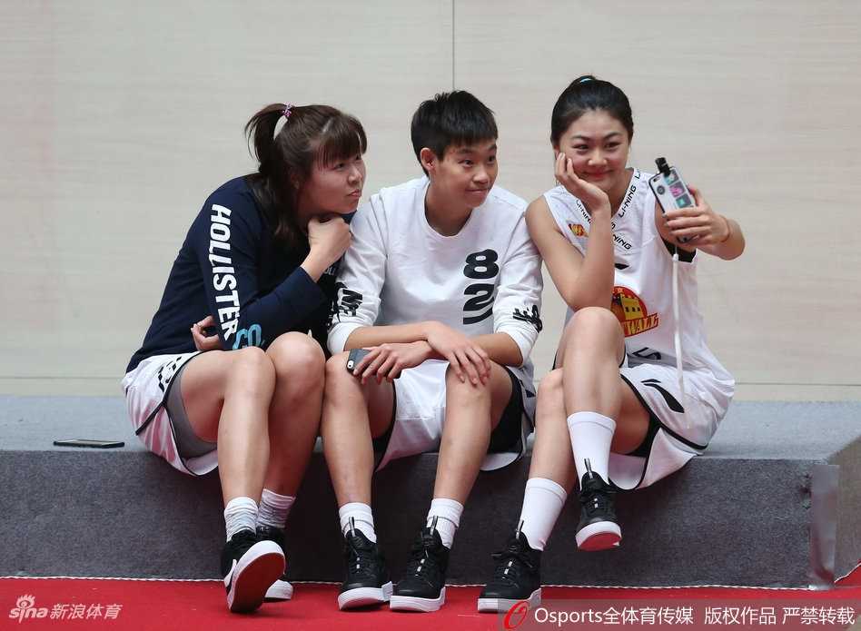 两名队员同框互动，一人搭着另一人的肩膀，相视而笑，默契十足。简单的白T恤搭配牛仔裤，却因她们青春洋溢的笑容而显得格外动人。