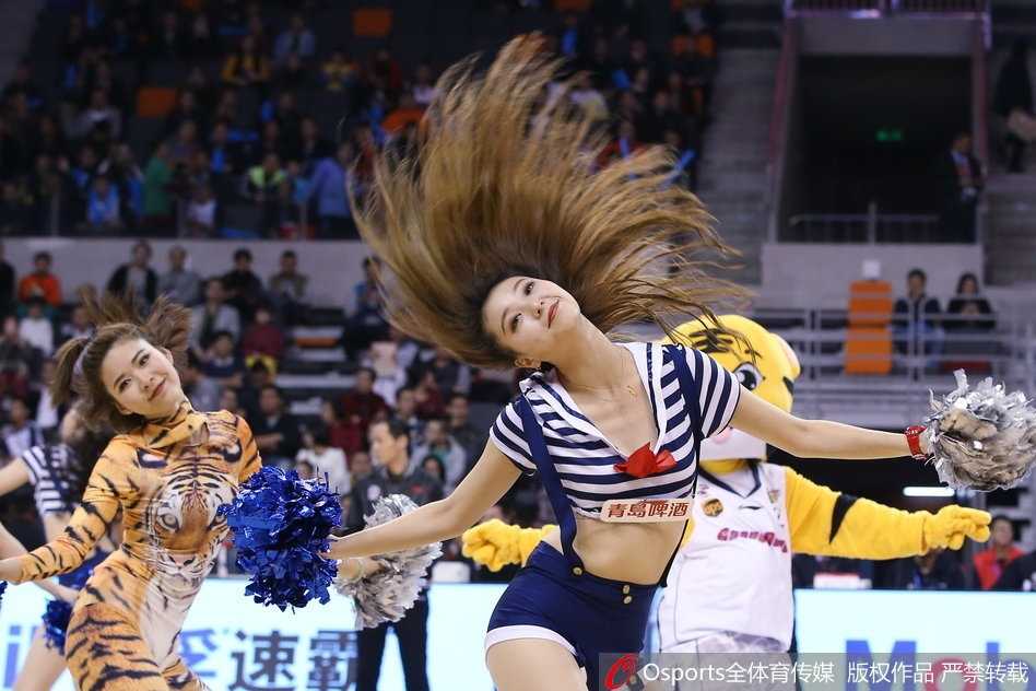 一名宝贝在表演间隙擦拭额头的汗珠，妆容依旧精致，眼神中透露出专注与疲惫，身后的大屏幕上正回放着易建联封盖对手的精彩瞬间，仿佛诉说着她们与比赛同在