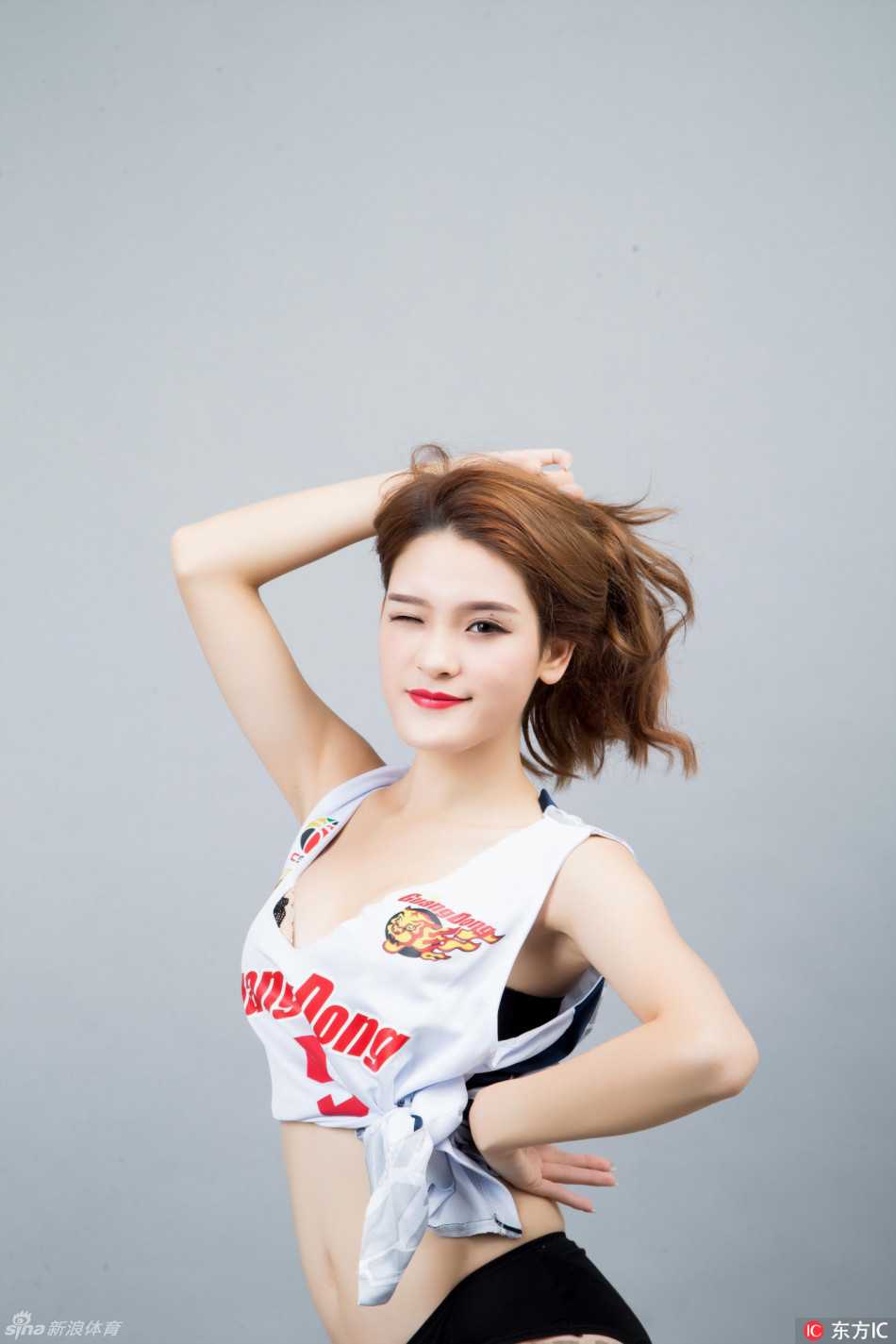 一位篮球宝贝在表演间隙看向镜头，精致的五官和甜美的笑容与背后激烈的比赛形成鲜明对比，展现出体育世界中刚柔并济的独特魅力。