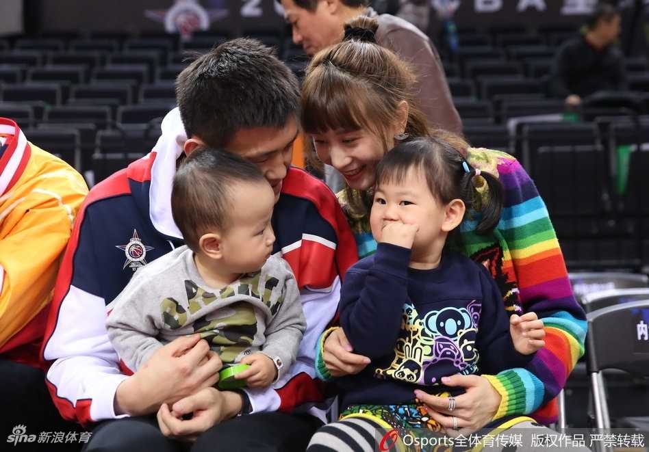 周鹏面带轻松的微笑抱着小儿子，刘美则陪伴在女儿身边，孩子们好奇地张望着球场上的激烈比拼，看台上的这一家子成了镜头追逐的焦点