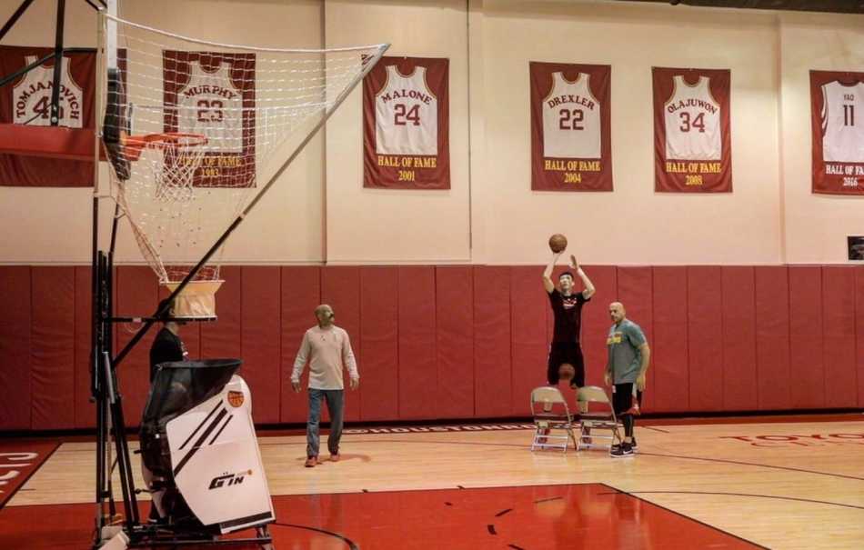 训练场上的周琦神情专注，正在完成一次投篮练习。阳光透过球馆的窗户洒在他身上，仿佛为他镀上了一层金色的光芒。从CBA到NBA，从新疆到休斯敦，他正脚踏实地，向着心中的篮球殿堂一步步迈进。