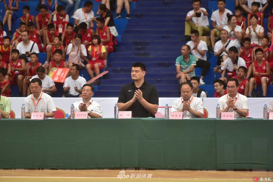 姚明站在领奖台前，双手郑重地将奖杯递交给一名身材瘦小的小球员，小球员双手接过奖杯，胸前的金牌闪闪发光，身后的队友们投来羡慕的目光