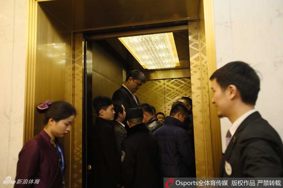 篮球巨人姚明身着深色西装挺拔而立，在武汉吉祥物入围仪式现场，他面带微笑看向远方，仿佛透过喧嚣看到中国篮球的光明未来。