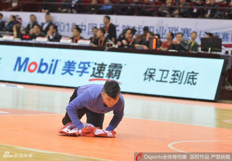 在聚光灯下，孟飞双膝跪地，用力而专注地擦拭着木地板上的汗渍，他的动作敏捷而有力，与身后静止的广告牌和紧张的比赛氛围形成鲜明对比