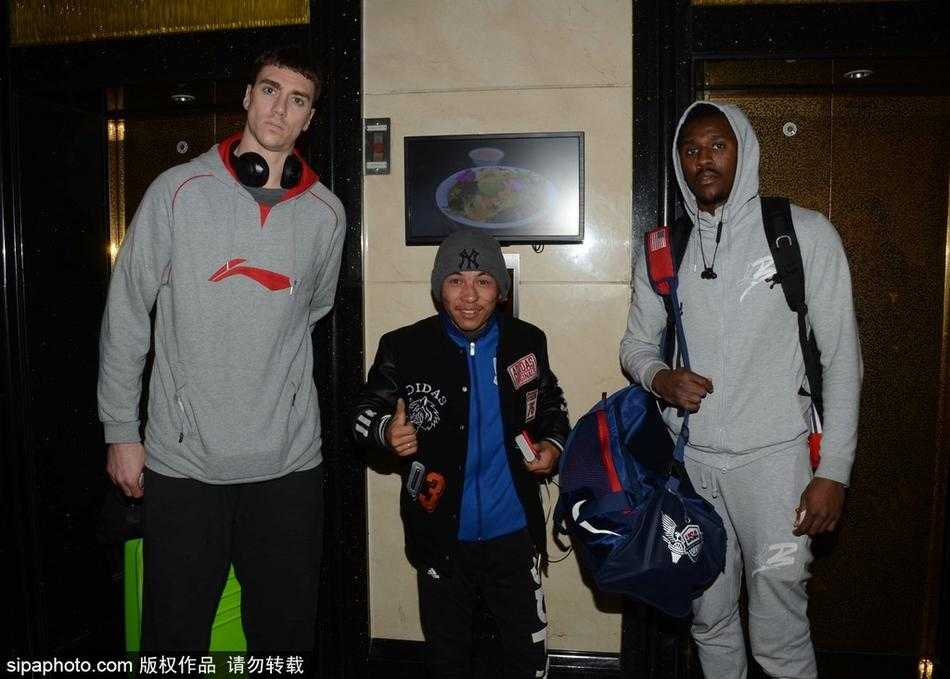 汉斯布鲁弯腰为小朋友在篮球上签名，周围球迷纷纷举起手机记录暖心瞬间