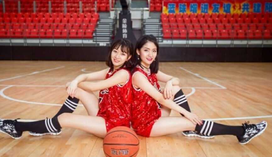 两位空姐篮球宝贝在赛前热身时默契击掌，一人身穿红色运动背心，一人身穿白色，健康的小麦色肌肤在阳光下闪着光。