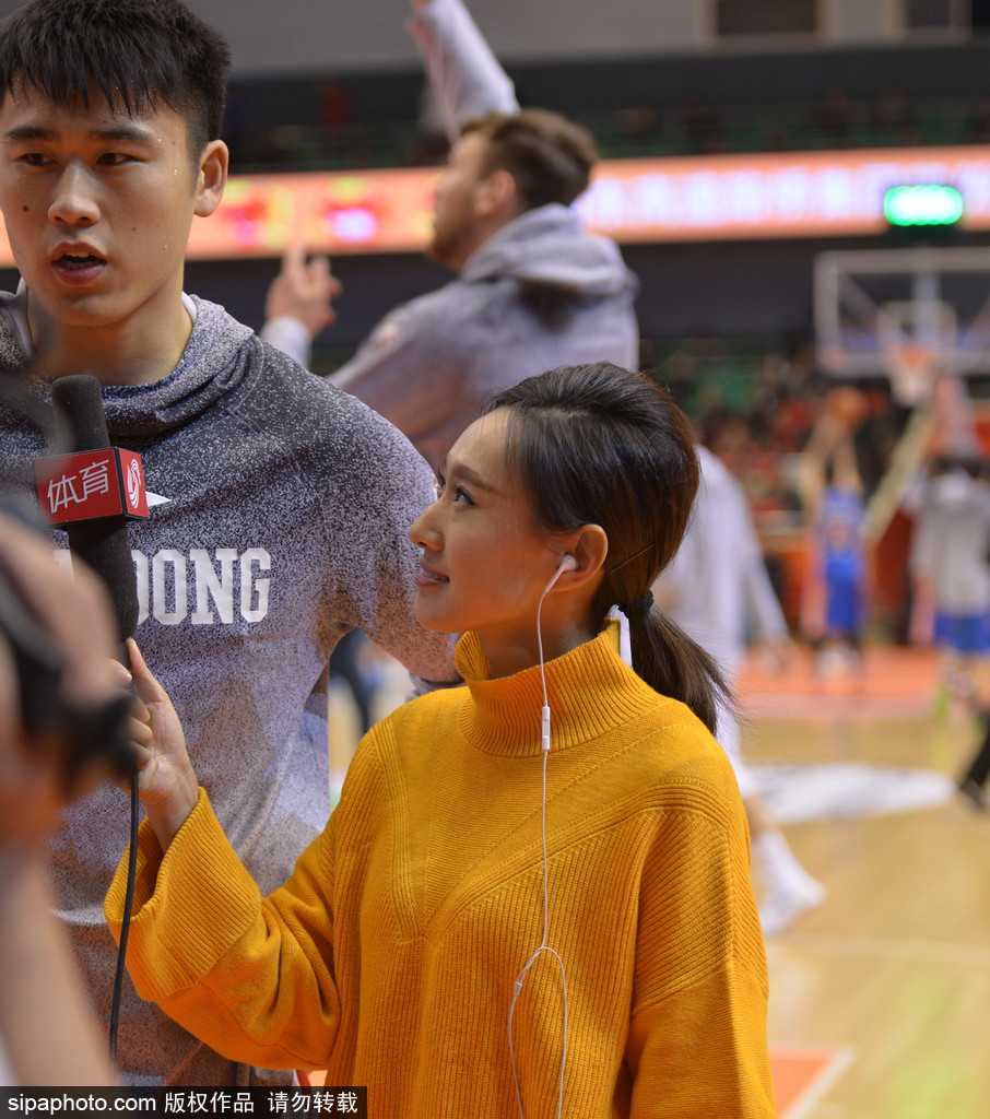 赛场灯光下，一位眉眼如画的美女记者双手紧握长焦相机，全神贯注地将镜头对准场内激战，她飘逸的长发与场内球员的汗水一同构成了冬夜里最动感的画面。