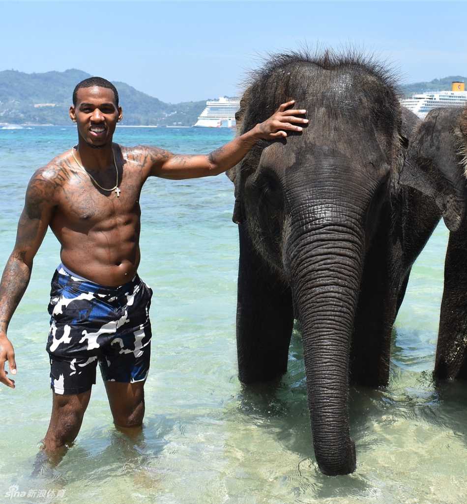 亚当斯站在一片开阔的水域旁，双手插兜，眺望远方。波光粼粼的水面映衬着他挺拔的背影，画面中充满了宁静与思考的意味。