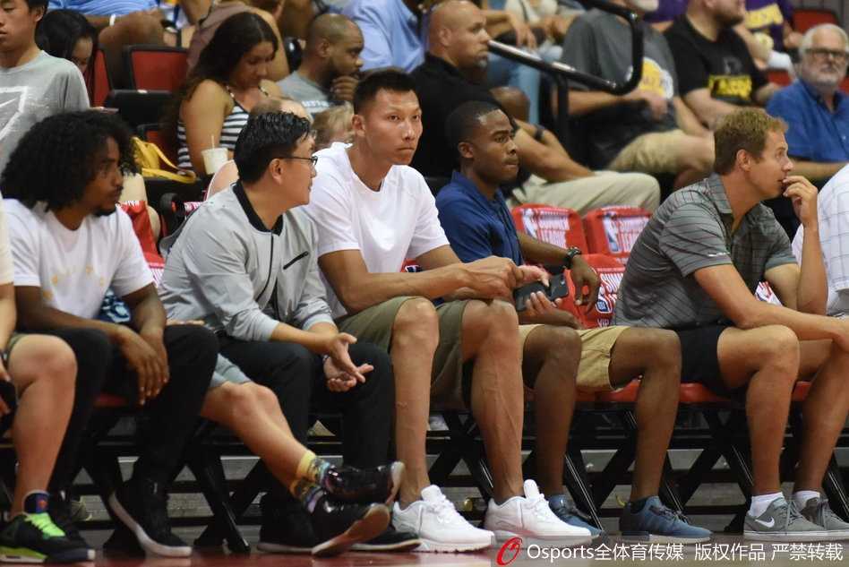 身穿浅色T恤的易建联神情轻松地坐在场边，目光柔和地望向赛场方向，仿佛一位老大哥在默默关注着弟弟的表现。